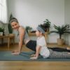 Mother doing on yoga mat with little daughter at home.