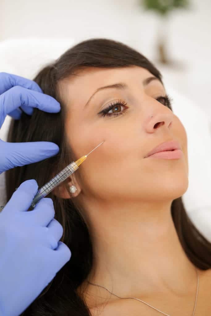 Female doctor injecting dermal fillers into woman's cheek.