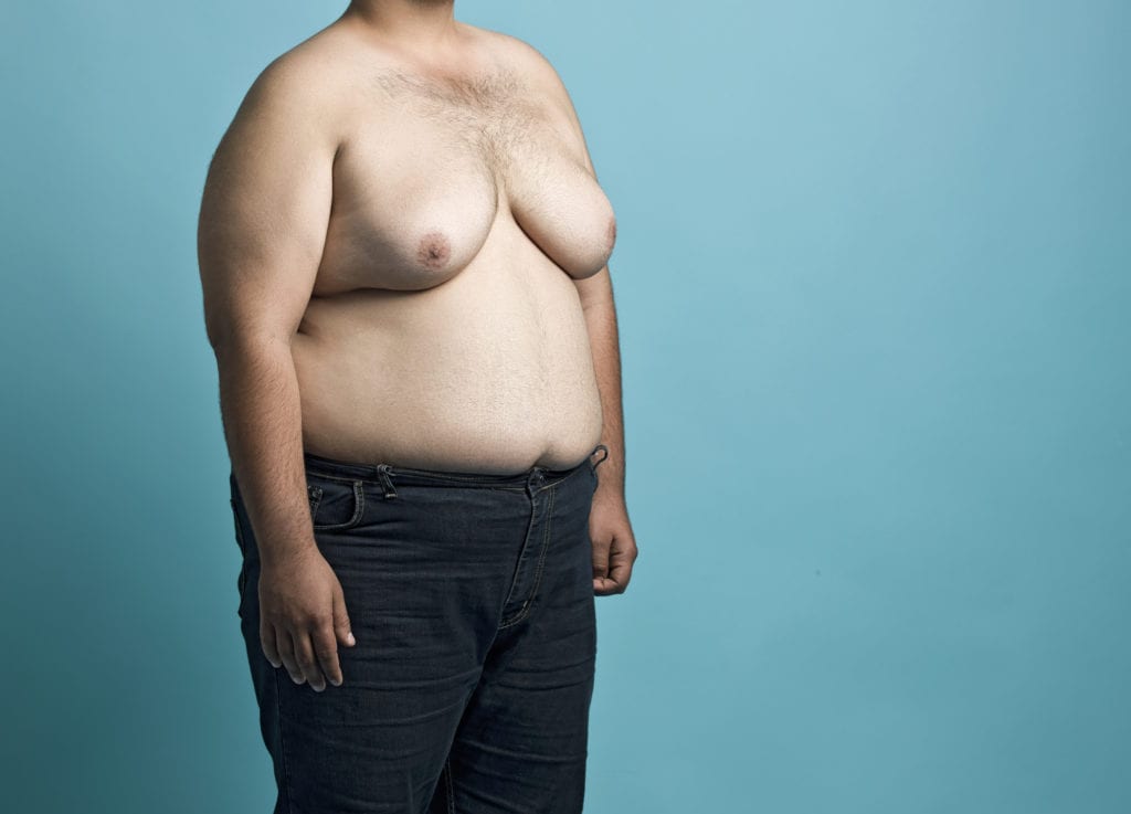 Obese young man with large breast on blue background.