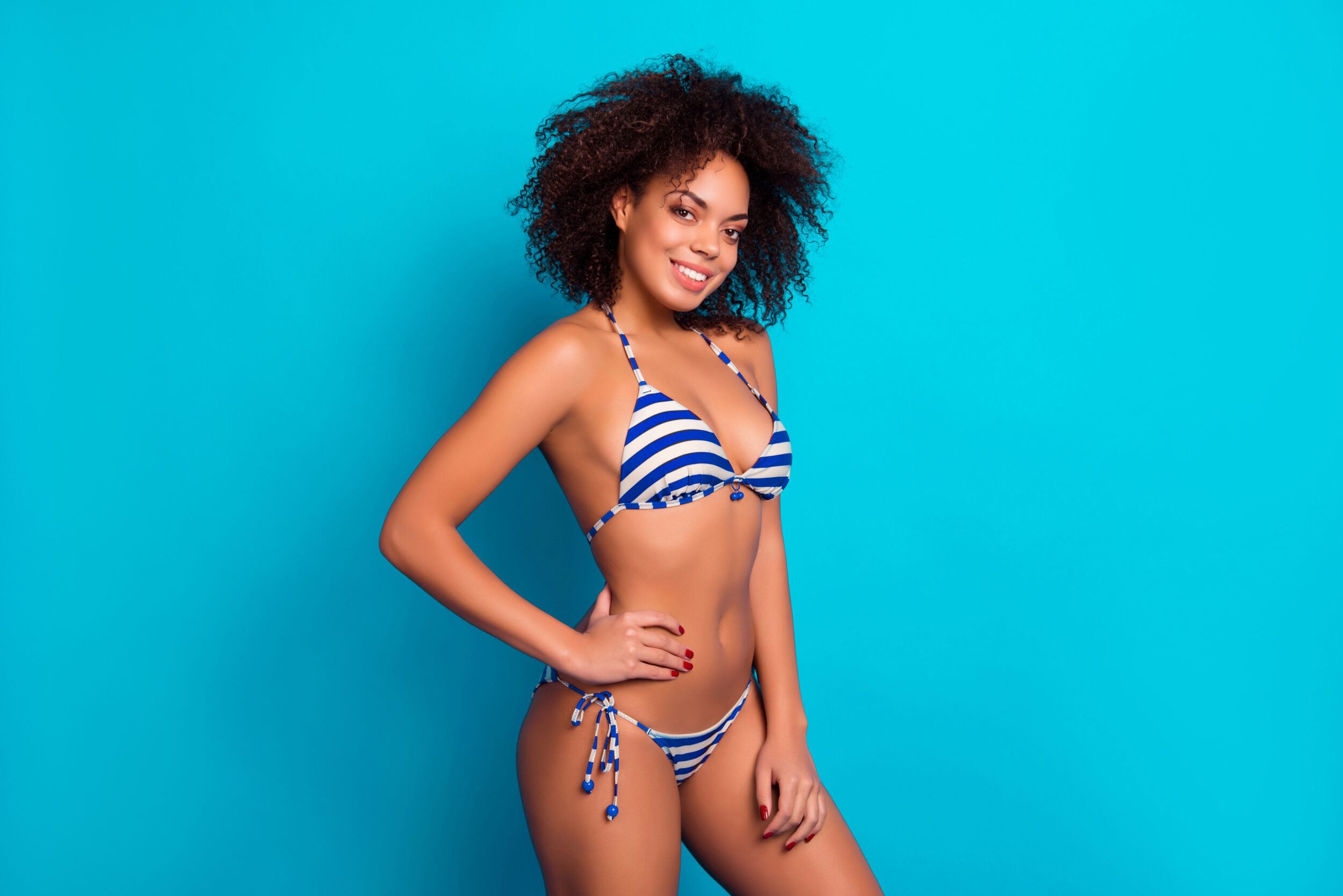 Woman in striped bikini poses to show off her rejuvenated figure thanks to breast augmentation with breast lift