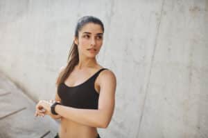 Jogging woman in sports bra checks her watch to monitor her running time.