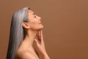 Woman has a new figure after significant weight loss. Asian woman with gray hair touches her smooth neck contours after SkinTyte.